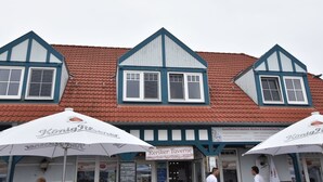 Een traditioneel gebouw met een rode dakbedekking en witte details. Twee witte parasols met daarop 'König Pilsener'. Een bordje met de tekst 'Reiker Tavern'.