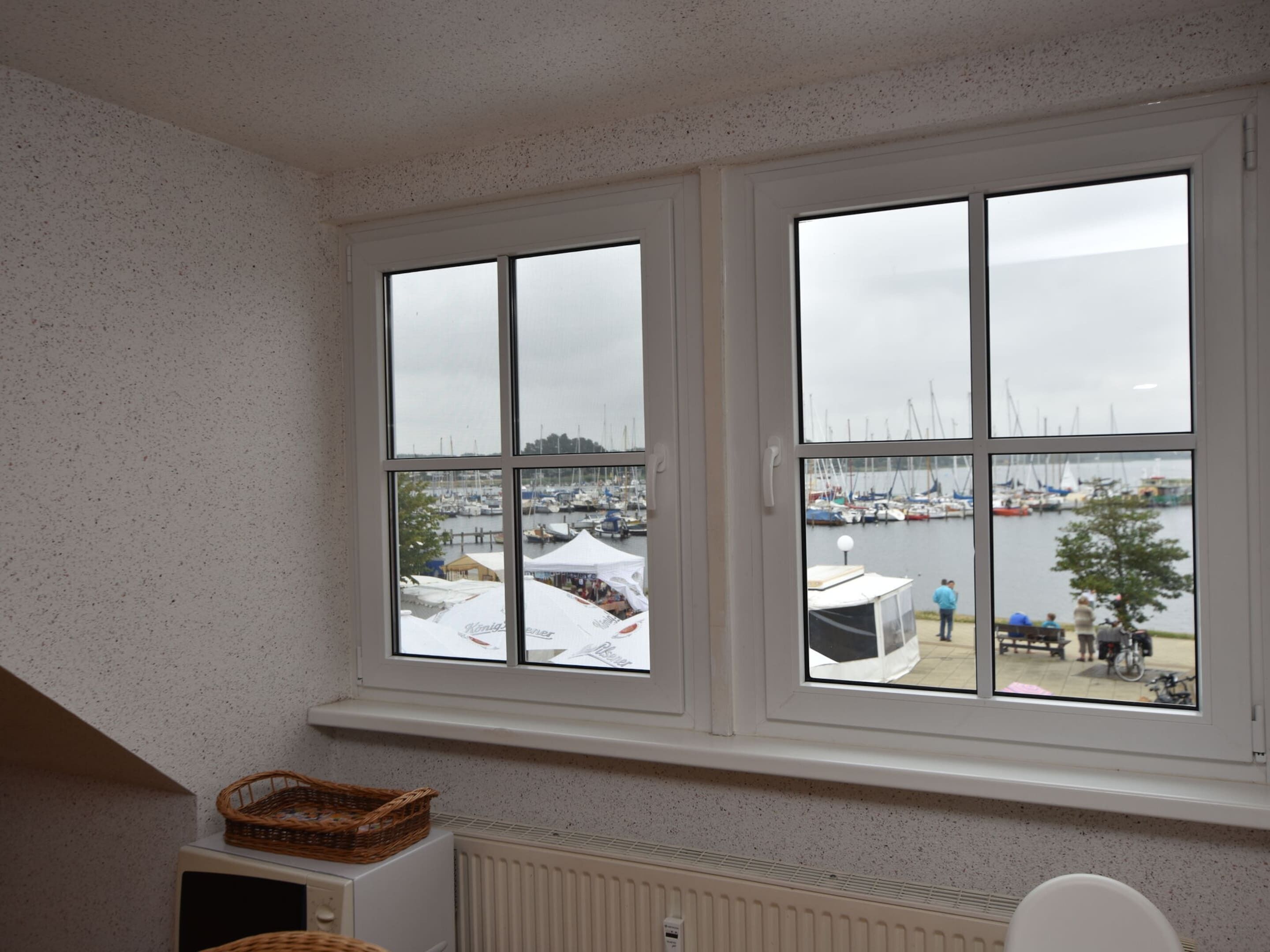 A room with a view of a marina through large windows, a radiator below, and a basket on the radiator.