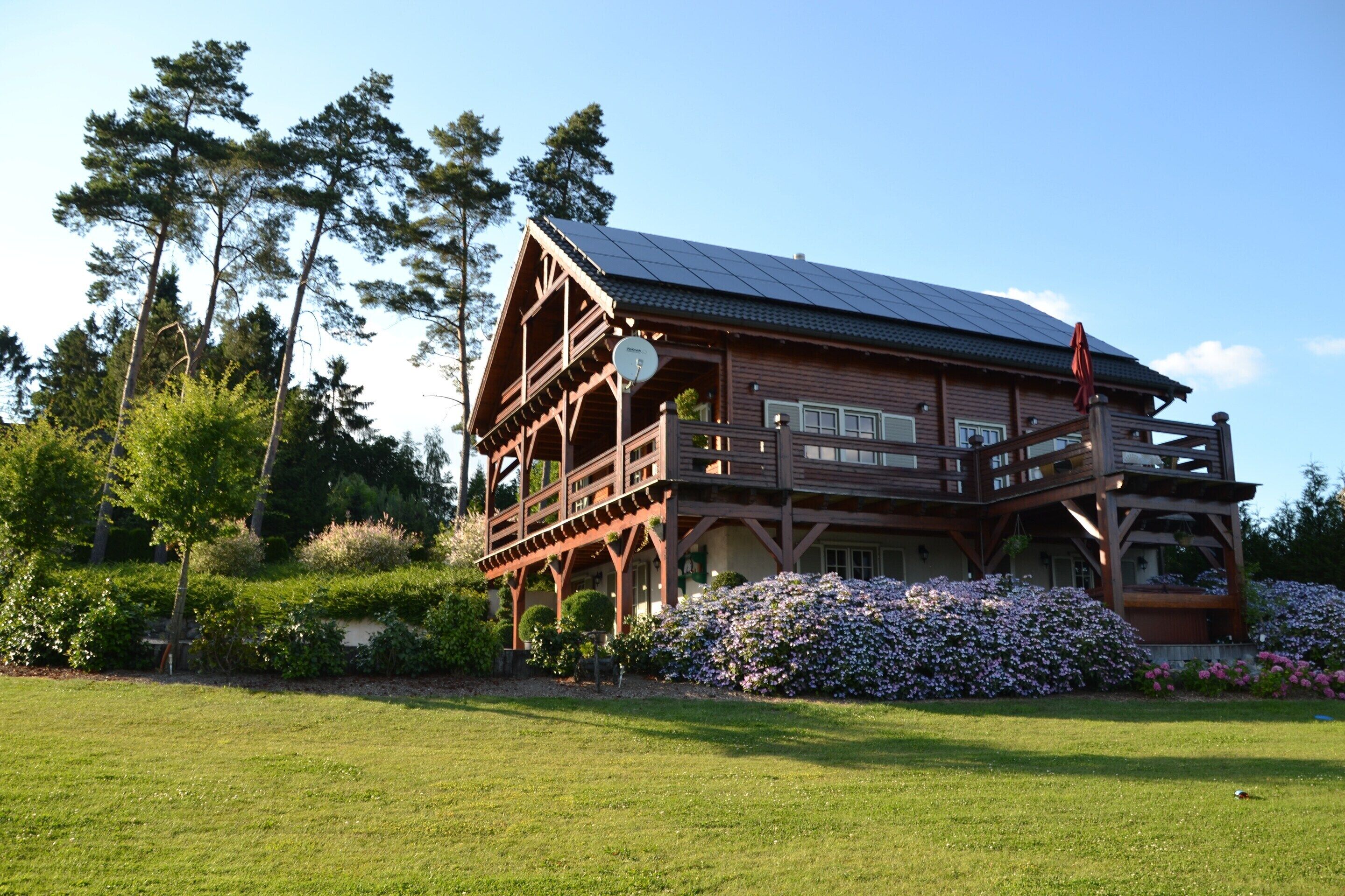 A wooden house with a balcony, surrounded by a well-maintained lawn and flowering bushes.