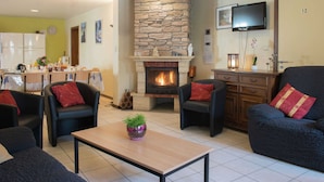 A living room with a stone fireplace, two sofas, a coffee table, and a TV mounted on the wall. - Child Friendly Holiday Home in Waimes with Sauna & Hot Tub (Waimes)