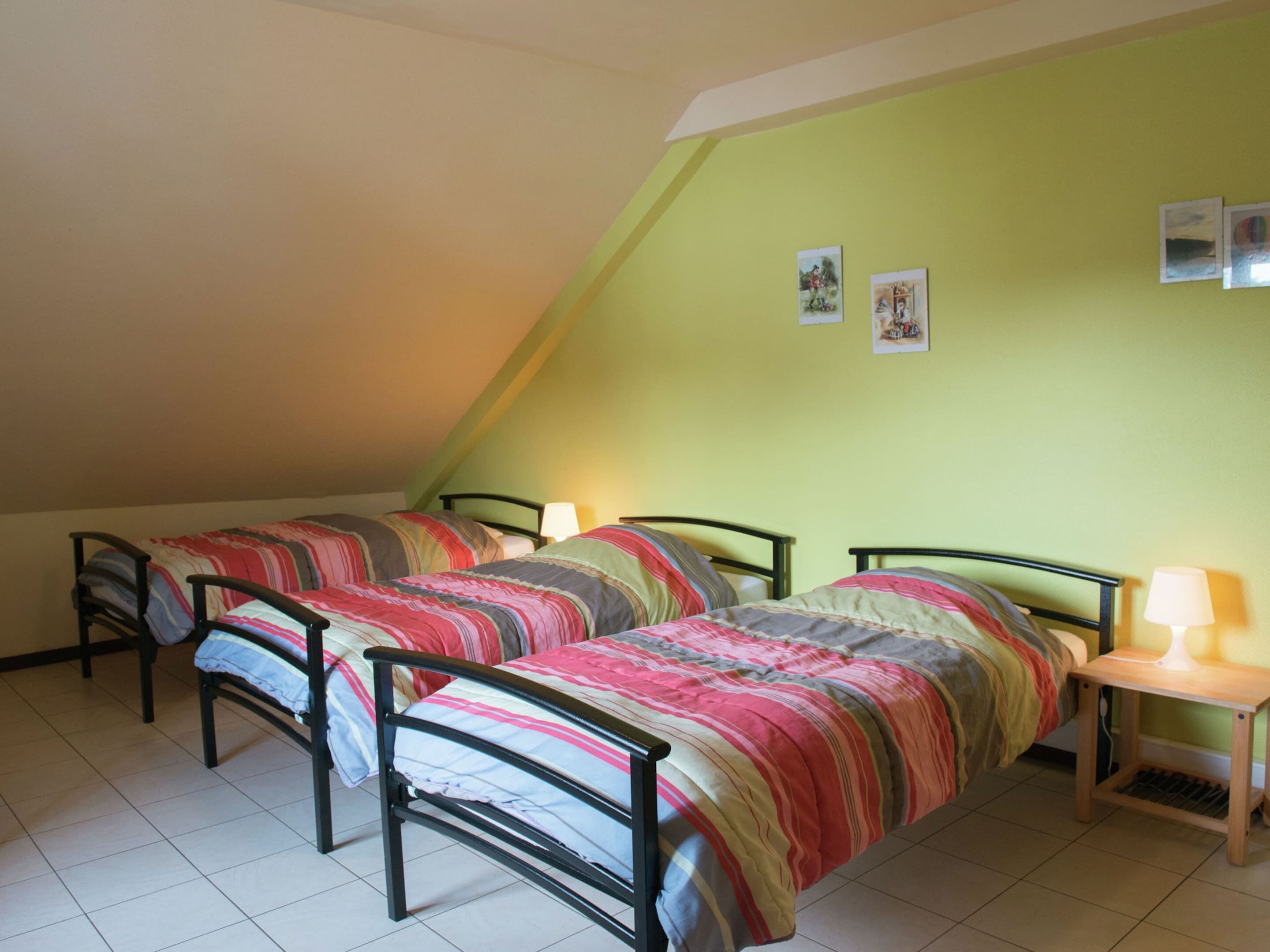 Un dormitorio con dos camas individuales, una mesita de noche pequeña con una lámpara y un techo inclinado.