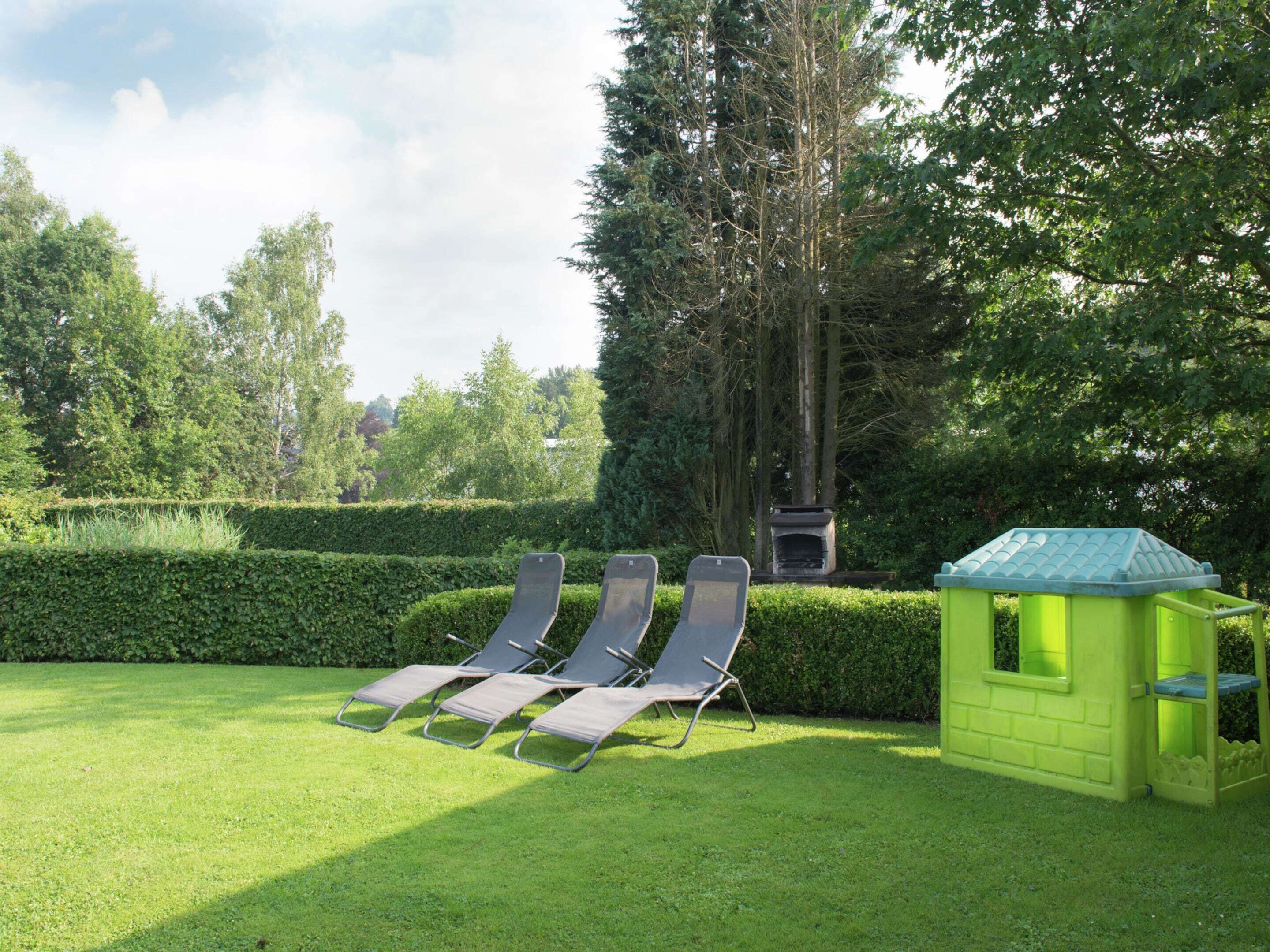 A garden with four lounge chairs and a small green playhouse.