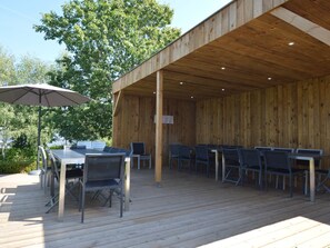 Eine Terrasse aus Holz mit Tischen und Stühlen, umgeben von Bäumen.