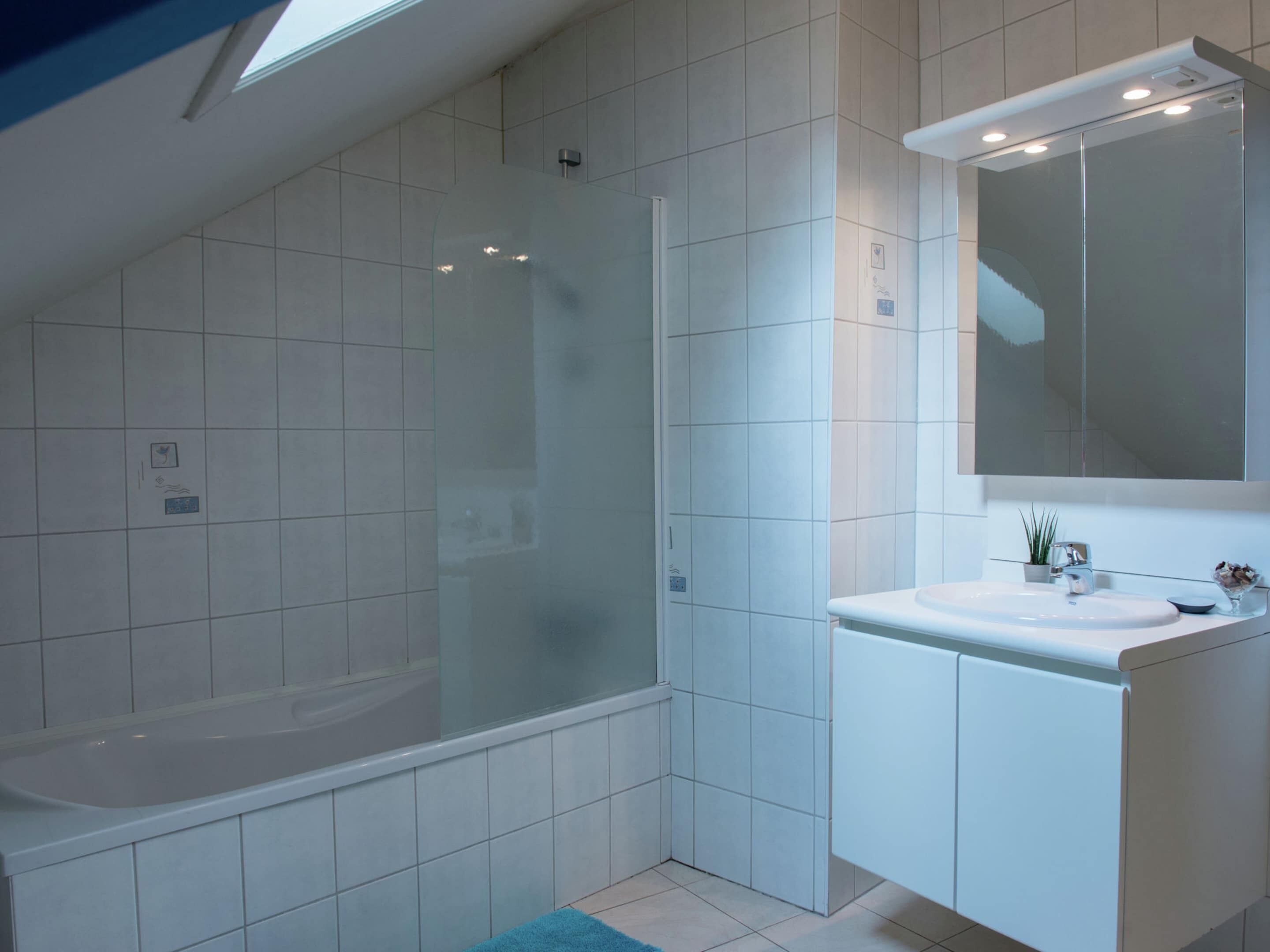 A modern bathroom with a glass-enclosed shower, a white sink, and a large mirror.
