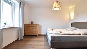 Een slaapkamer met een bed, een dressoir, een raam en een hangende lamp.