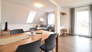 Een moderne woonkamer met een houten eettafel, zwarte stoelen, een grijze bank en een groot raam met gordijnen.