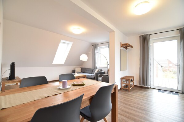 Un salon moderne avec une table à manger en bois, des chaises noires, un canapé gris et une grande fenêtre avec des rideaux.