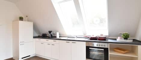 A modern kitchen with white cabinets, a built-in oven, a coffee maker, and a window above the sink.