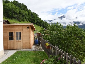 A wooden cabin with a wooden door and windows, a small porch, and a view of a green hillside and mountains in the background. - Apartment Near Pizol (Landquart)