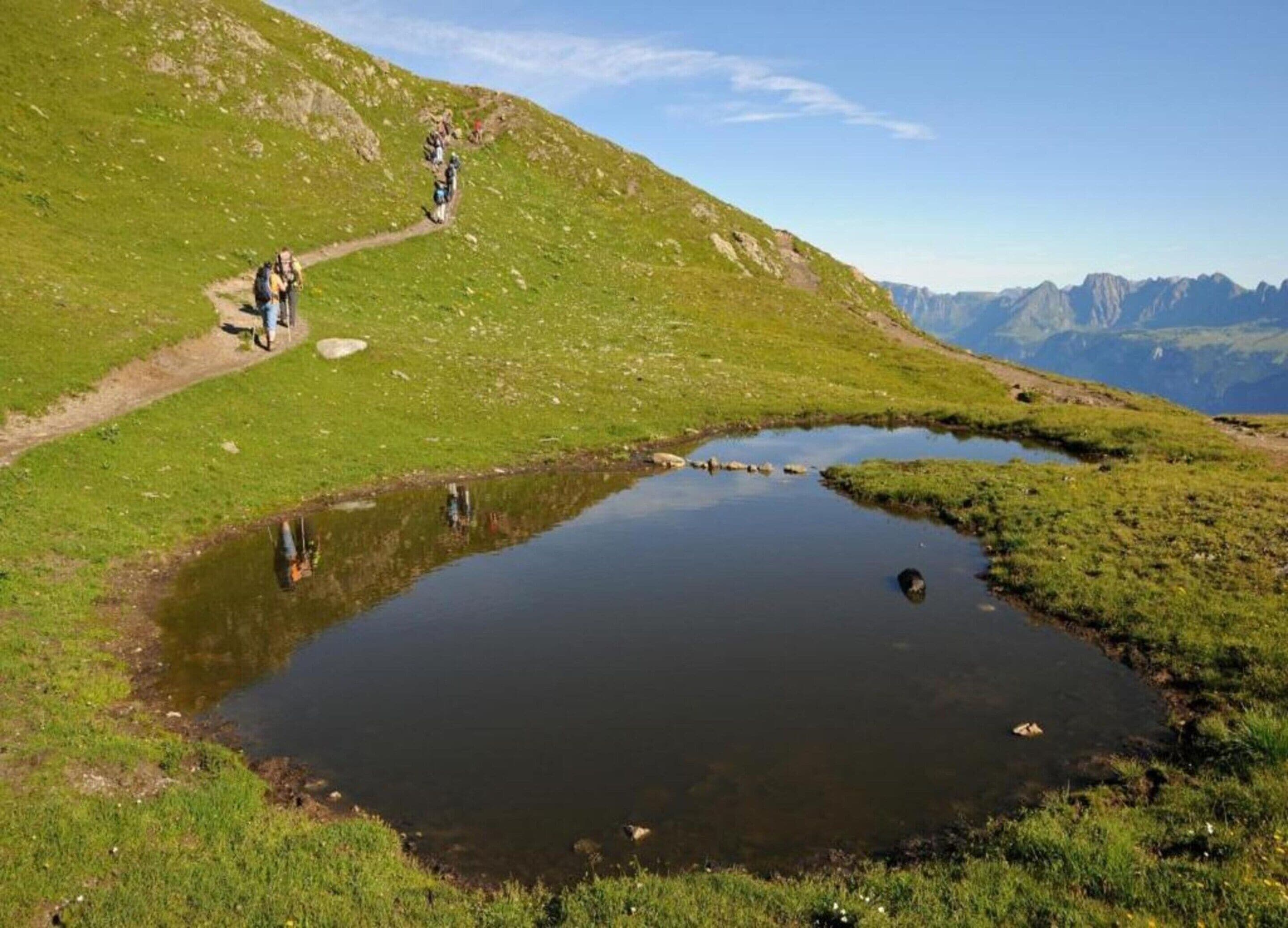 Un paysage montagneux avec un petit étang et un sentier de randonnée.
