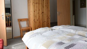 Une chambre à coucher comprenant un lit, une armoire en bois, une chaise et une porte donnant sur une autre pièce.