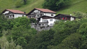Un ensemble de bâtiments de style chalet, dotés de balcons, se dressant sur un fond de verdure luxuriante et d’une colline.