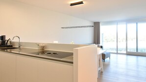A modern kitchen with a central island, a built-in sink, and a dining area with a sofa and table. - Bright Coastal Family Escape (De Panne)