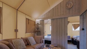 A cozy room with a wooden ceiling, a sofa with multiple cushions, a wooden coffee table, and a bed in the background. - Cozy Tent Lodge in Pittem With Veranda,barbecue (Pittem)