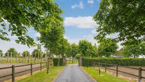 A gravel driveway leading to a gated entrance surrounded by trees and hedges. - Cozy Tent Lodge in Pittem With Veranda,barbecue (Pittem)