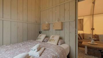 Una habitación acogedora con una cama, dos almohadas con el texto 'BE HAPPY', un banco de madera y una pequeña mesa.