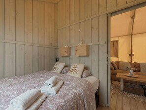 Een knus ingerichte kamer met een bed, twee kussens met de tekst 'BE HAPPY', een houten bankje en een klein tafeltje.