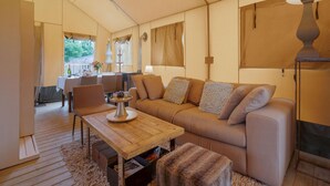 A cozy living room with a sofa, coffee table, and a fireplace. There is a dining area with a table and chairs, and a view of the outdoors through large windows.