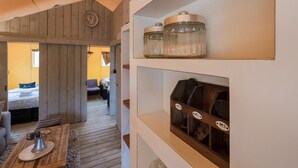 A cozy room with wooden walls, a bed with a blue pillow, a wooden coffee table, and shelves with jars and a wooden chest. - Cozy Tent Lodge in Pittem With Veranda,barbecue (Pittem)