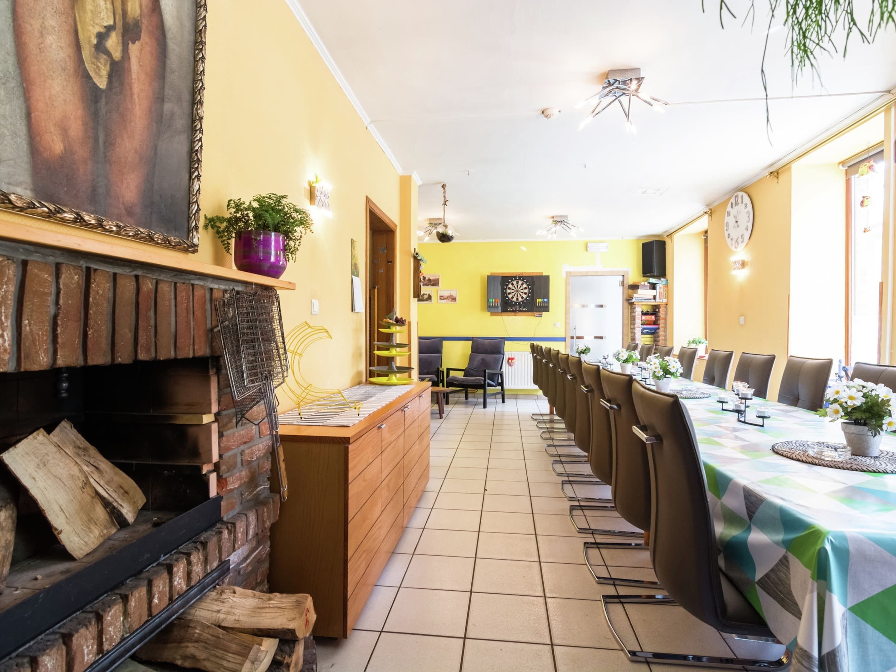 A dining area with a long table, chairs, a fireplace, and a dartboard.