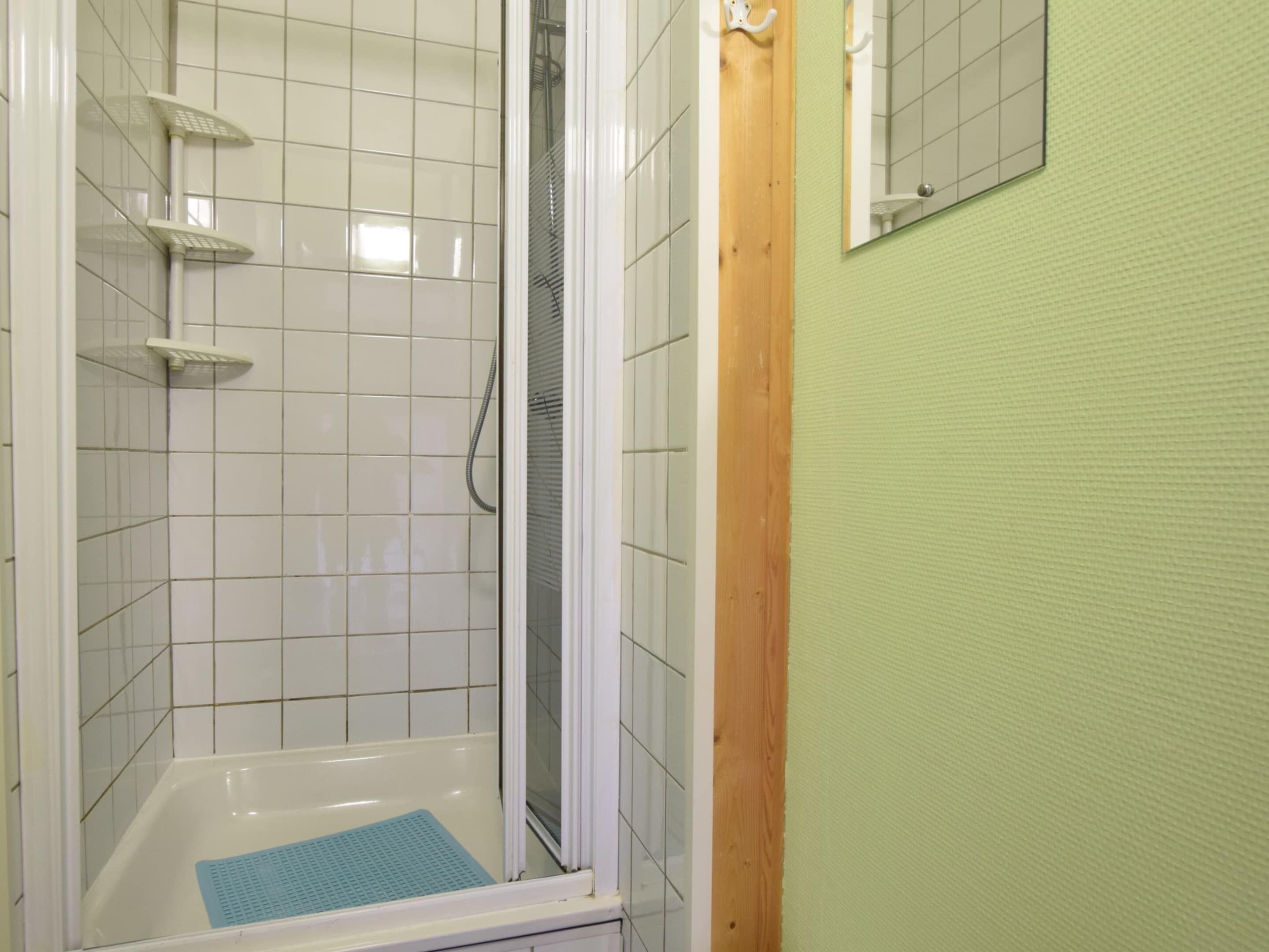 A bathroom with white tiled walls, a shower with a glass door, and a wooden door frame.