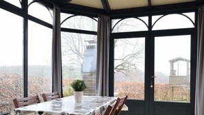 A conservatory with a table covered in a Paris-themed tablecloth, surrounded by wooden chairs. - Lovely Spot With Plenty of Outdoor Space (Sainte-Ode)