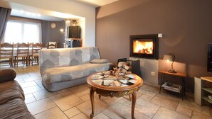 A living room with a sofa, a coffee table, a fireplace, and a dining area with chairs and a table. - Lovely Spot With Plenty of Outdoor Space (Sainte-Ode)