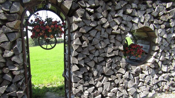 A stone archway with a wheel and flower boxes. - Lovely Spot With Plenty of Outdoor Space (Sainte-Ode)