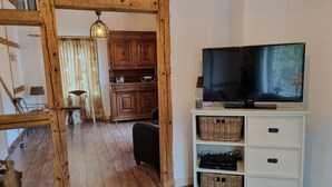 Ein Wohnzimmer mit Holzboden, einer Fernsehung auf einem weißen Schrank und einer Holzbalkendecke.