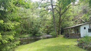 Ein rustikales Blockhaus mit Fluss im Hintergrund, umgeben von dichtem Wald.