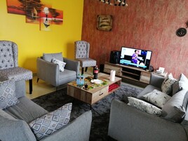 A living room with a sofa set, a coffee table with items, a television, and artwork on the walls.