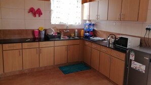A compact kitchen with wooden cabinets, a sink, a microwave, and a refrigerator. - Yurana Resort Kenya (Kitengela)