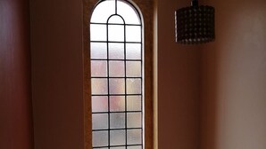 A room with a tall, narrow window with a grid pattern, a hanging light fixture, and a potted plant on the floor. - Yurana Resort Kenya (Kitengela)