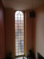 A room with a tall, narrow window with a grid pattern, a hanging light fixture, and a potted plant on the floor.