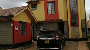 A two-story building with a red and yellow facade, a black SUV parked in front, and a paved driveway. - Yurana Resort Kenya (Kitengela)