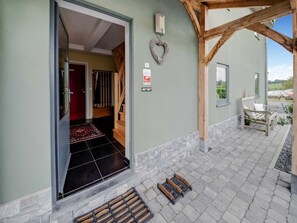 A building entrance with a wooden porch, a red door, a heart-shaped decoration, and a bench outside. - Ardennes View Apartment- Petit Wilogne (Houffalize)