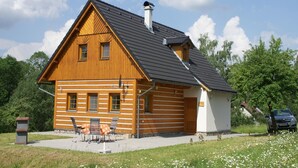 A wooden log cabin with a sloped roof, a chimney, and a small porch with chairs.