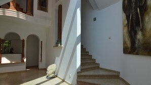 Een ruim interieur met een trap, een stenen beeldhouwwerk en een groot schilderij.