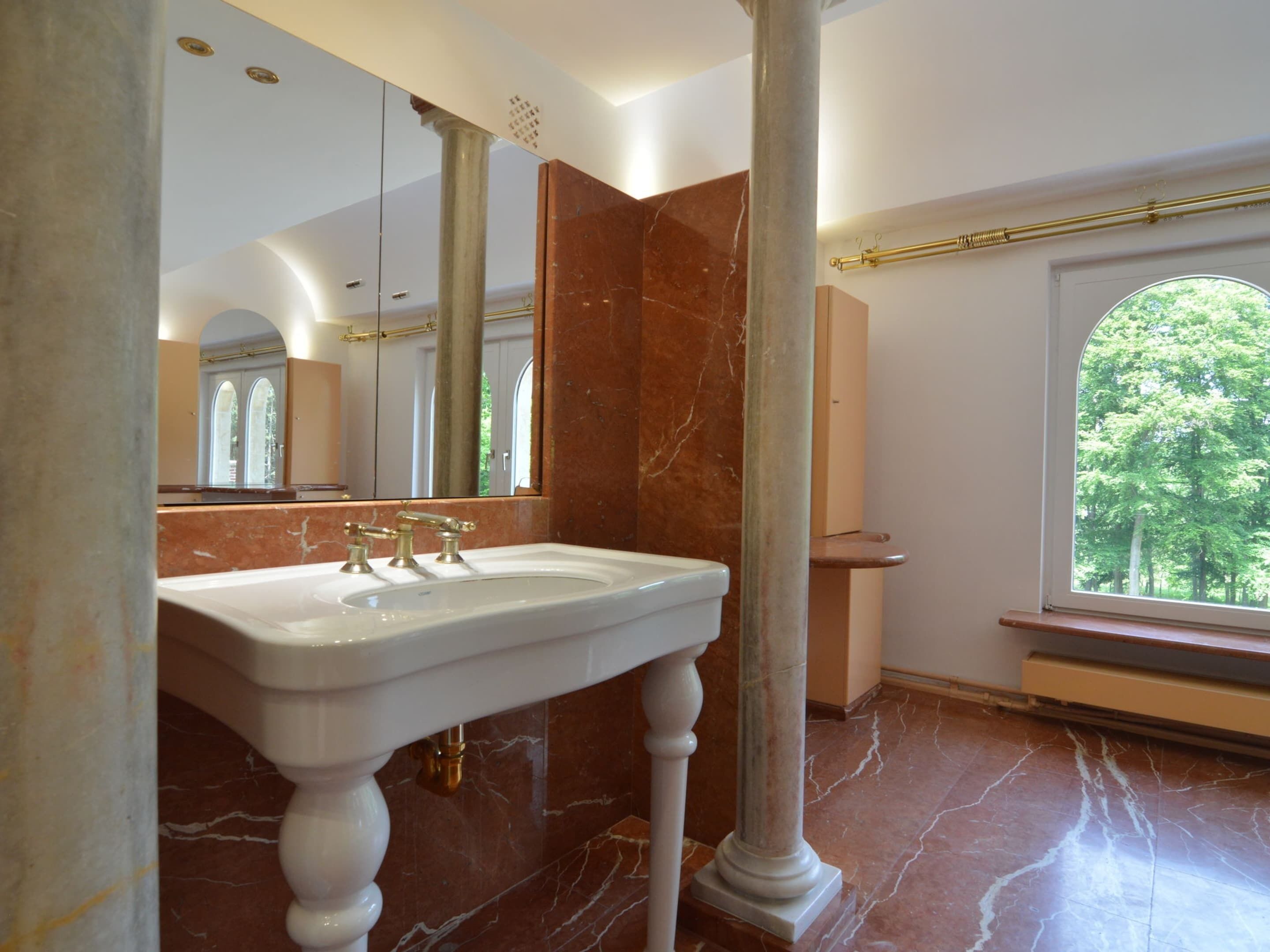 Un baño con un lavamanos grande de mármol, un espejo y una ventana con vistas a árboles.
