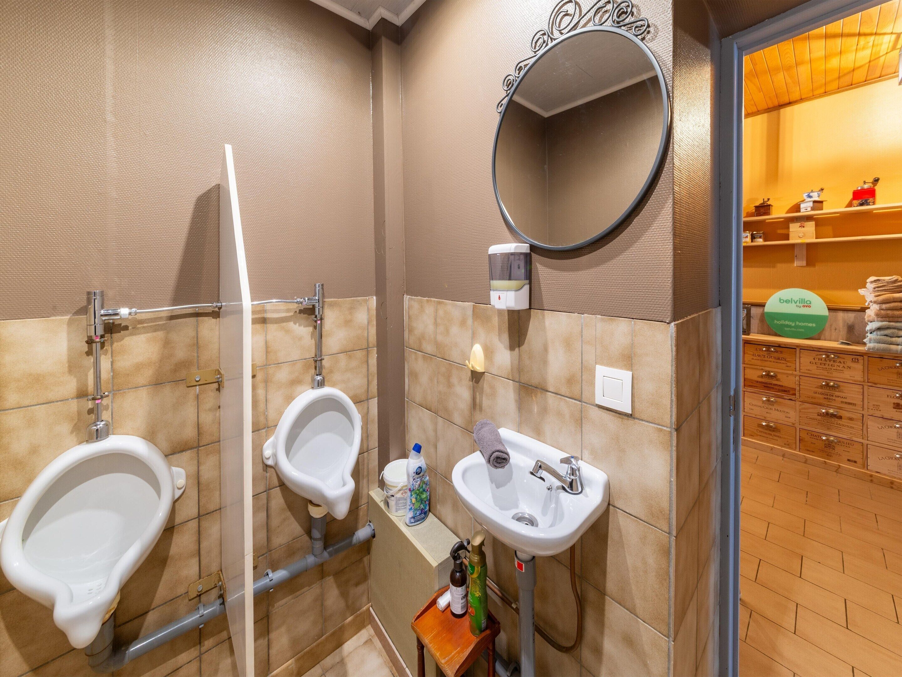 Baño con dos orinales, un lavabo y un espejo. Hay un toallero con toallas y un dispensador de jabón.