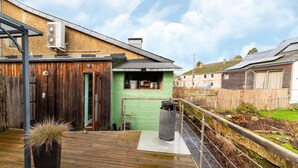 En træterrasse med en potteplante, en grøn væg og en metalfad.
