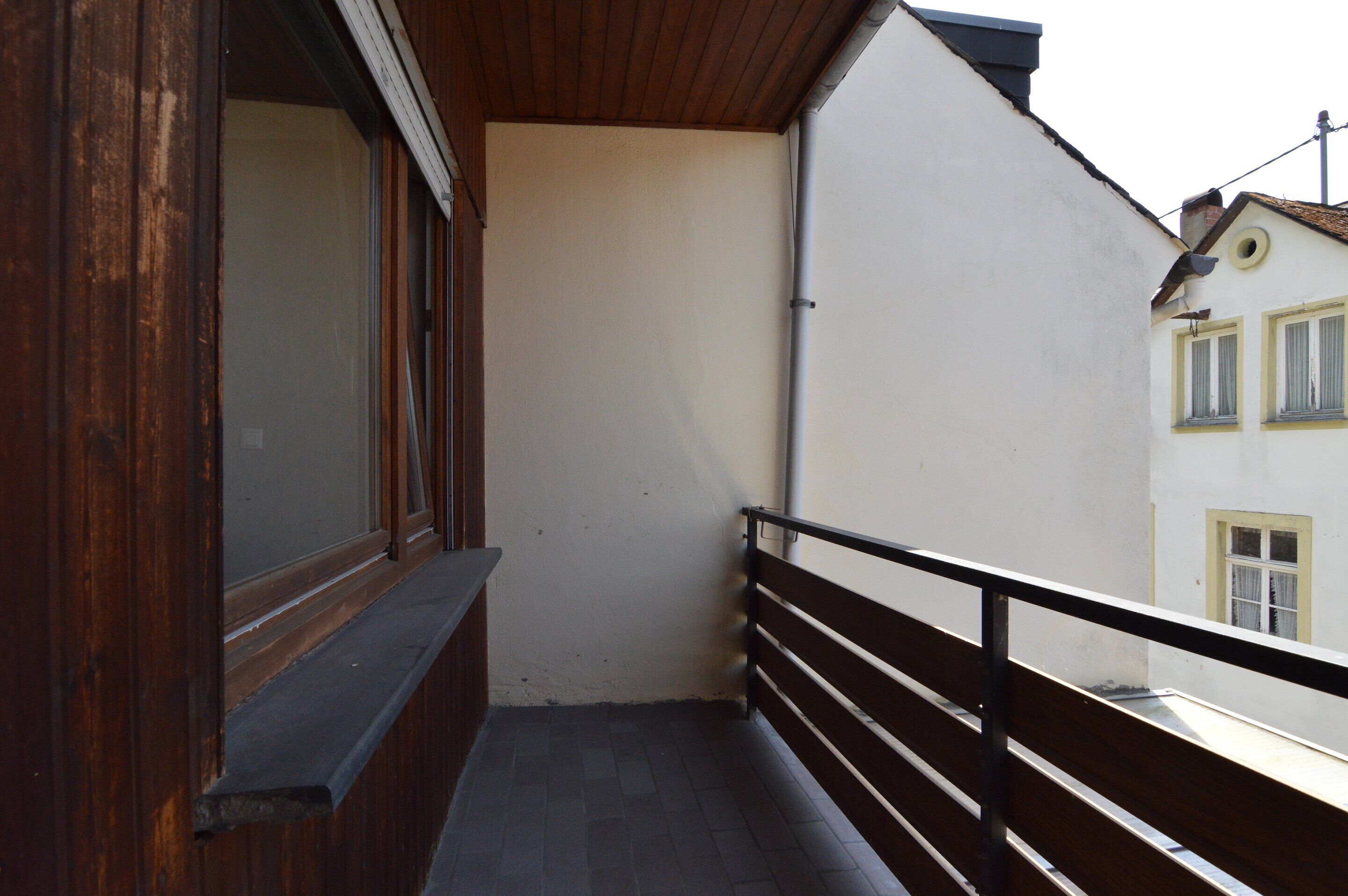 Een balkon met een houten hekwerk, een raam en een witte muur.