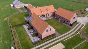 Un grand bâtiment rectangulaire en briques, surmonté d’un toit en tuiles, entouré de pelouses bien entretenues et d’un petit étang.