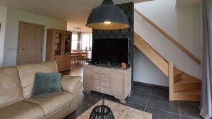 A living room with a sofa, a cabinet, a TV, and a staircase. - Holiday Home in Alveringem Near Beach (Alveringem)