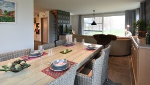 A dining area with a long table, wicker chairs, and a view of the outdoors. - Holiday Home in Alveringem Near Beach (Alveringem)