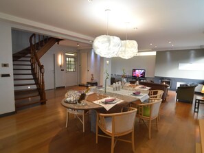 Un vaste espace dédié à la salle à manger, avec un escalier en bois, une cheminée et un téléviseur en arrière-plan.