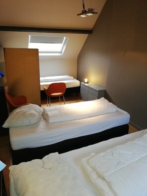 Une chambre avec un puits de lumière, un lit avec une literie blanche, une chaise rouge et un bureau avec une lampe.