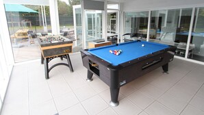 A modern indoor recreational area with a pool table, foosball table, and glass-enclosed patio. - Beautiful Villa for Groups With Swimming Pool, Sauna and Wifi (Zottegem)