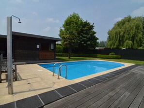 Une piscine avec une terrasse en bois, un espace bar et un coin salon abrité.
