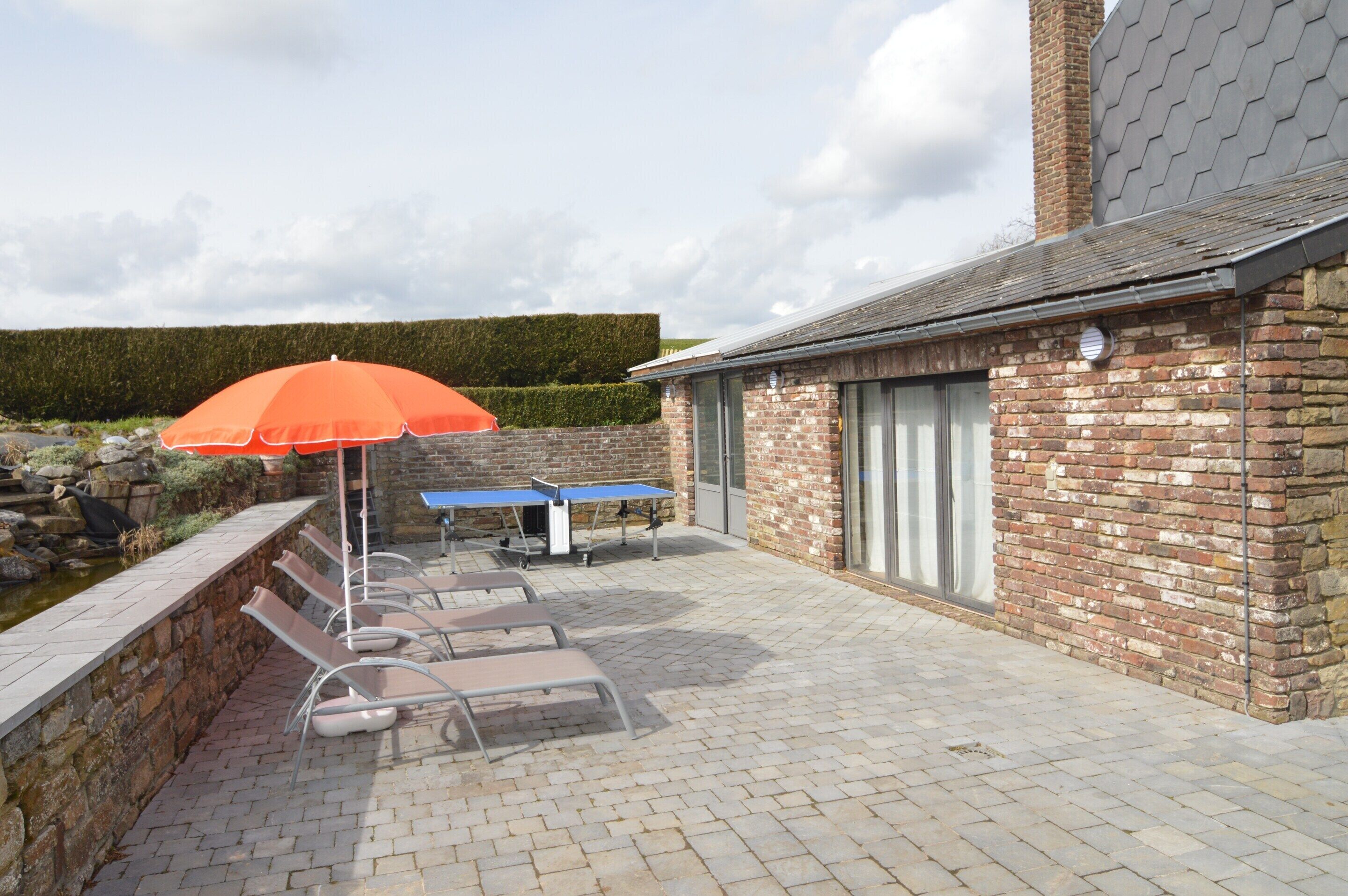 A patio with lounge chairs, a table, and an umbrella.